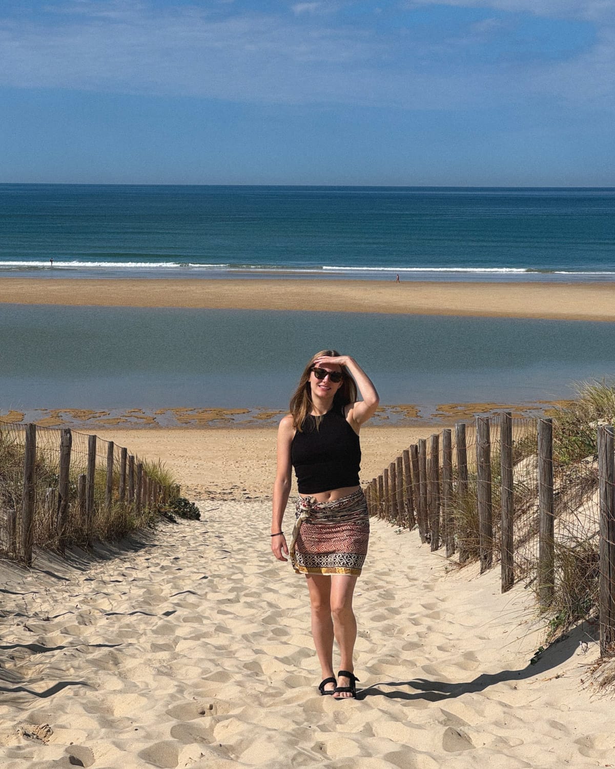 Cec walking down a sandy path away from the beach in Cap Ferret, shading her eyes.