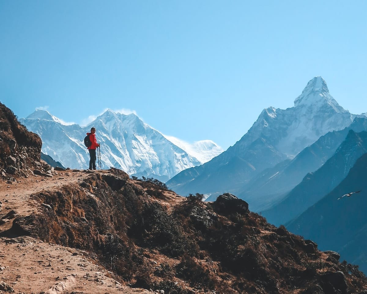 Cec standing on a rugged trail in Nepal, with towering Himalayan snow-capped peaks in the distance.