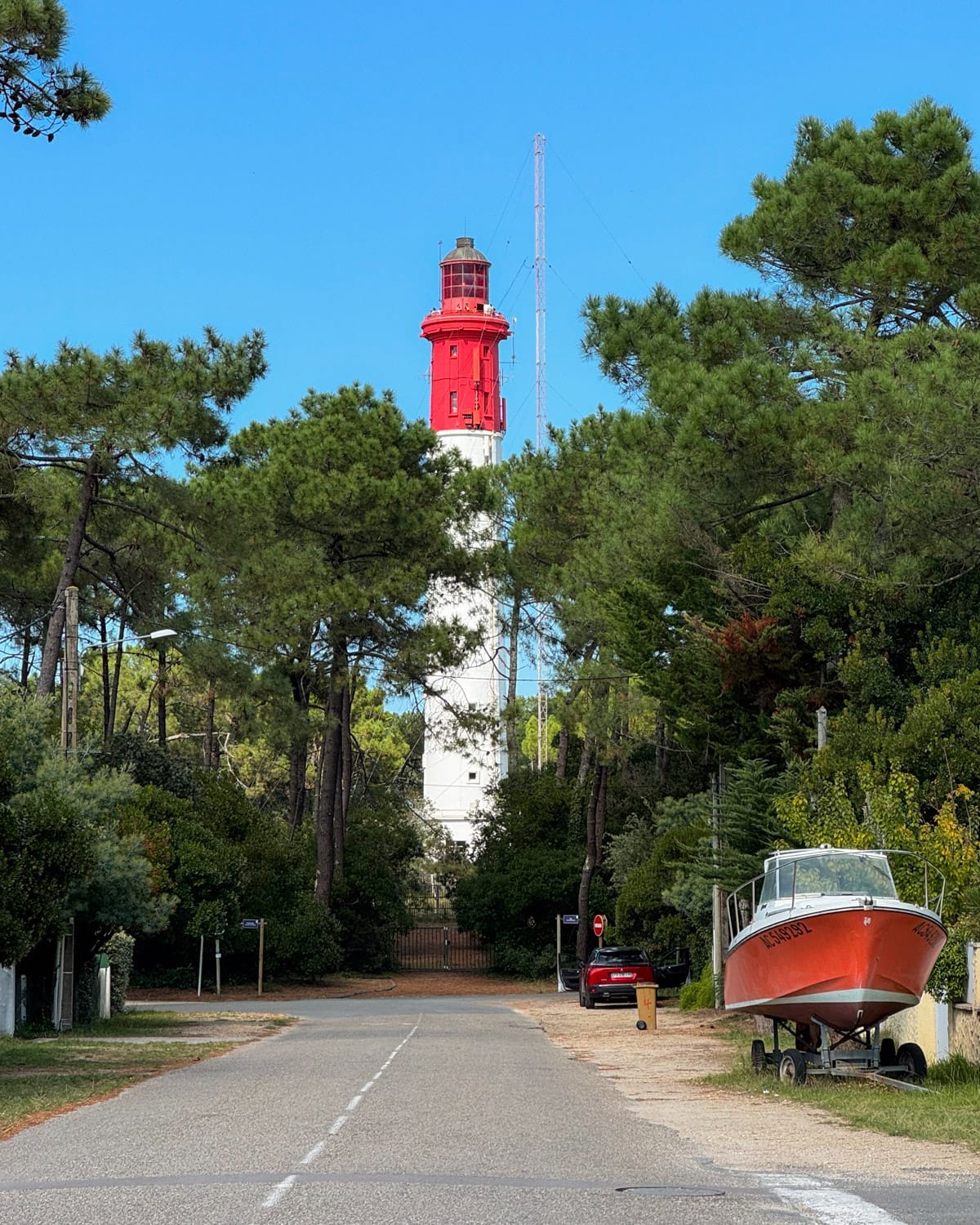  The Cap Ferret Lighthouse with its red and white tower, framed by green pine trees, on a clear blue-sky day.