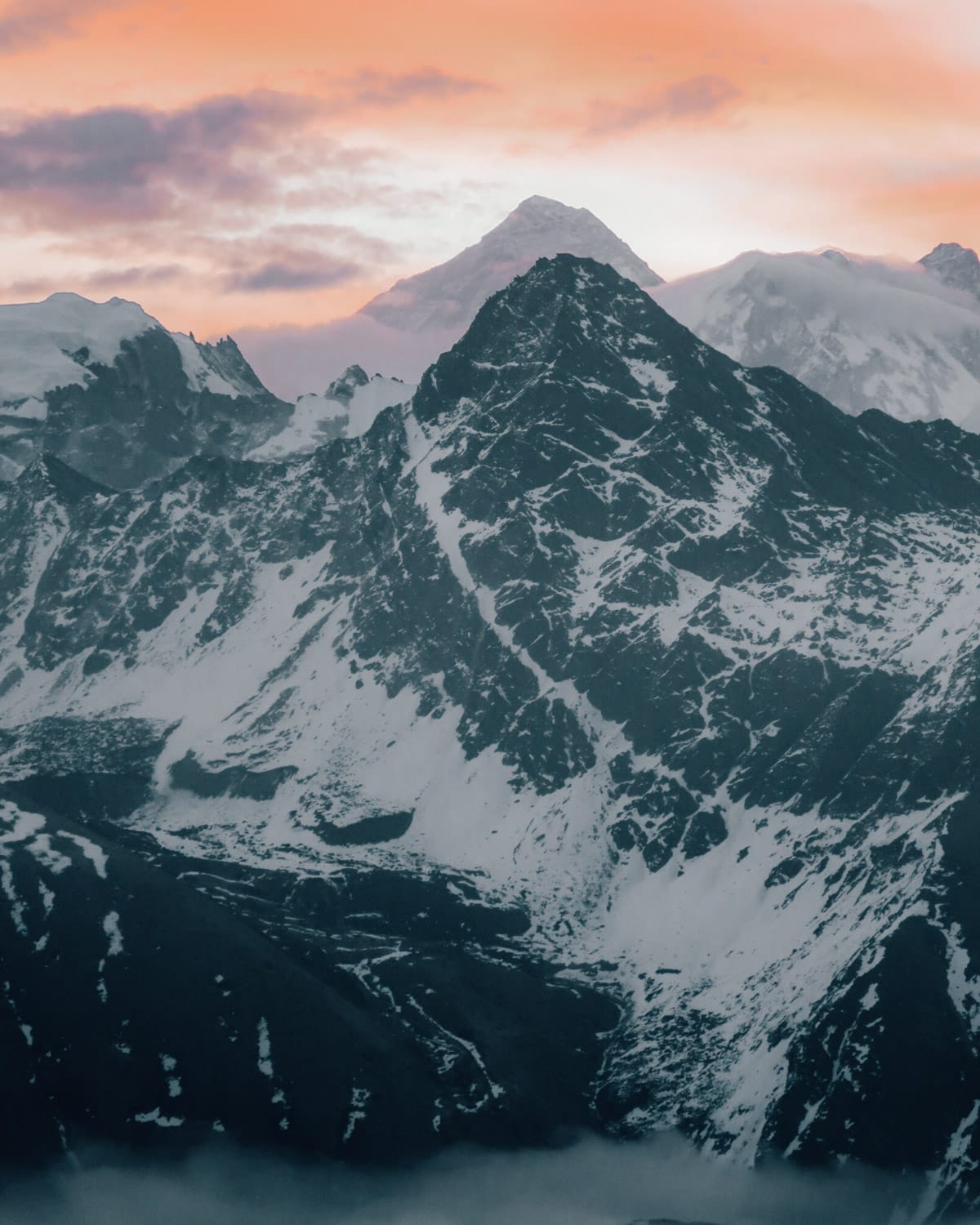 Mount Everest glows softly at sunset behind rugged snowy peaks during the ascent up Gokyo Ri.