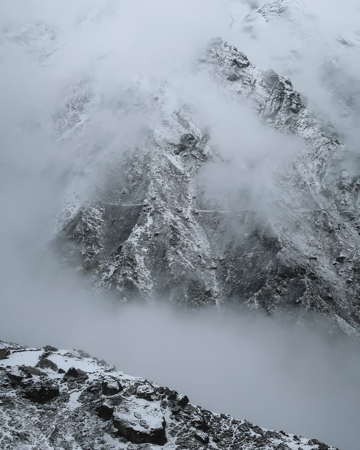 Snow-covered cliffs partially veiled by clouds along the Gokyo Ri trek route in the Himalayas.