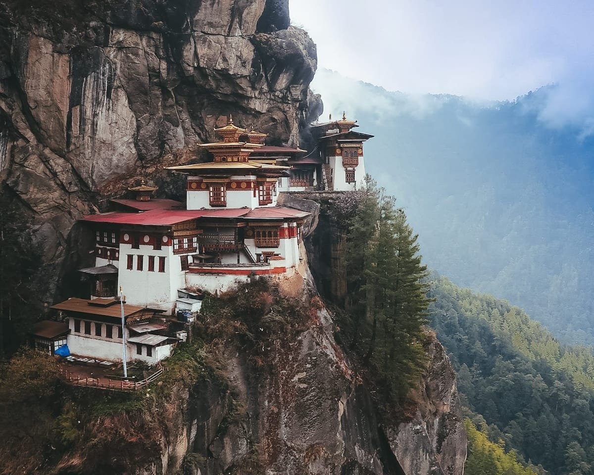 The sacred Tiger's Nest Monastery clings to a steep cliffside, surrounded by misty mountains and dense forest.