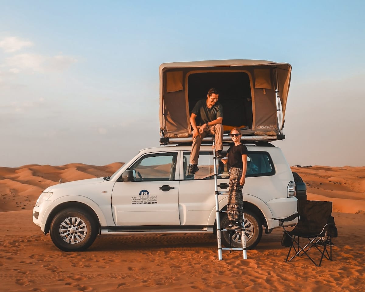 A rooftop tent on a 4x4 vehicle, with Cec and Ari preparing for an overnight stay in the golden sand dunes of Oman..