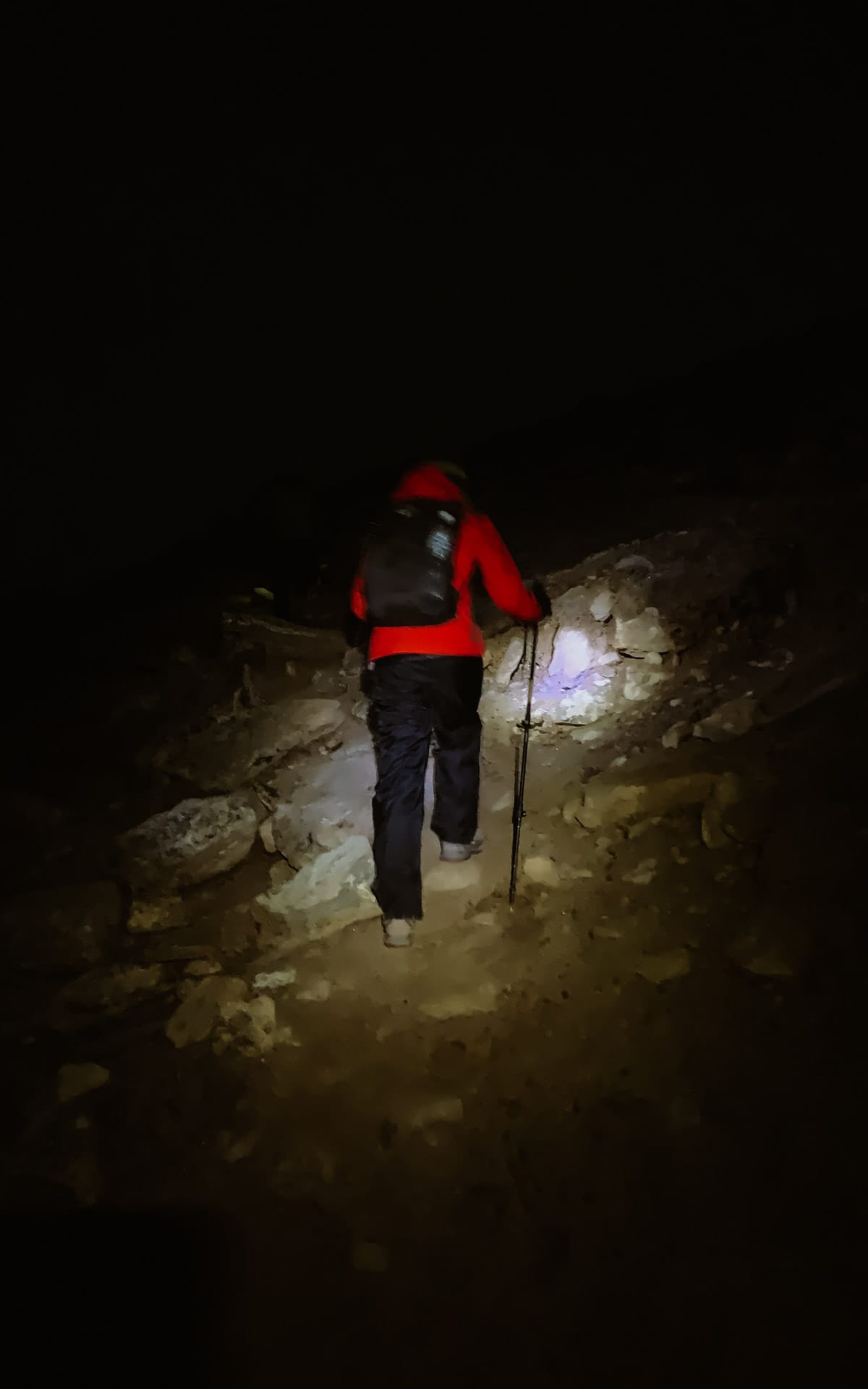 Cec with a headlamp and poles climbs a rocky trail up Gokyo Ri in complete darkness before sunrise.