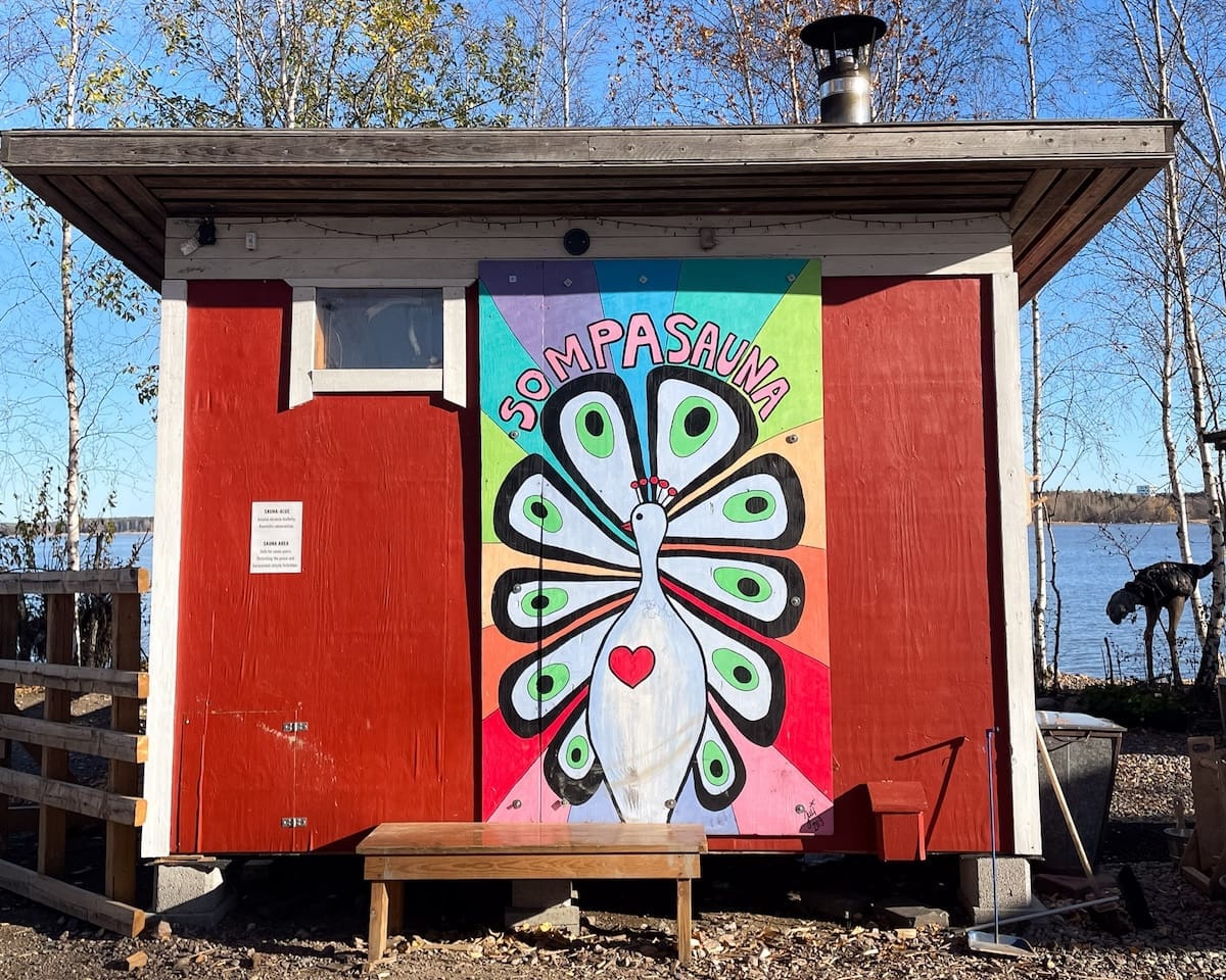 A red sauna hut with a painted peacock mural near the water at Sompasauna in Helsinki.