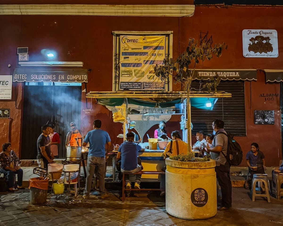 People gather around a street food stand in Oaxaca, illuminated by warm streetlights.
