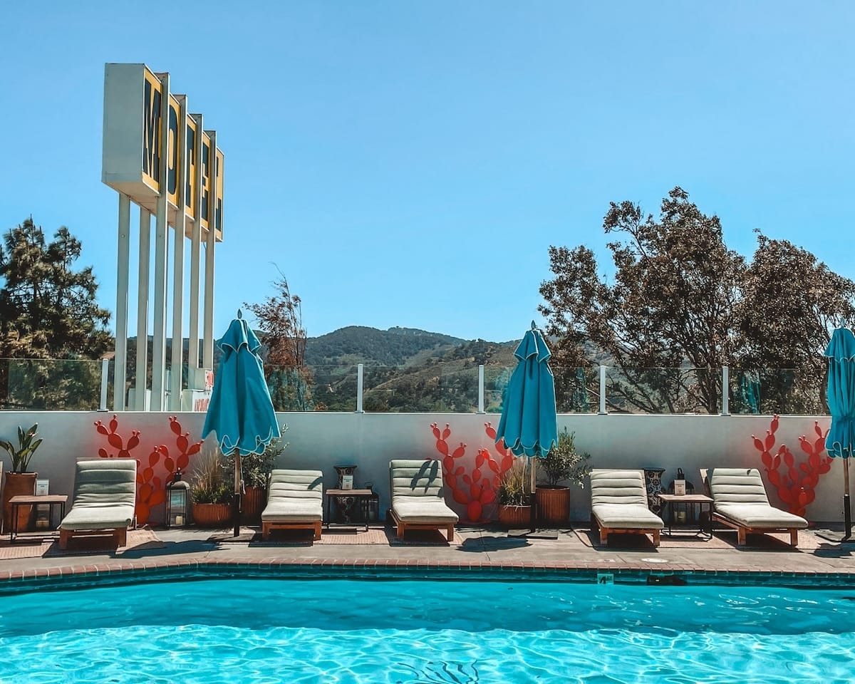 Lounge chairs and blue umbrellas surround a pool with a vintage "Motel" sign in Los Alamos, California..