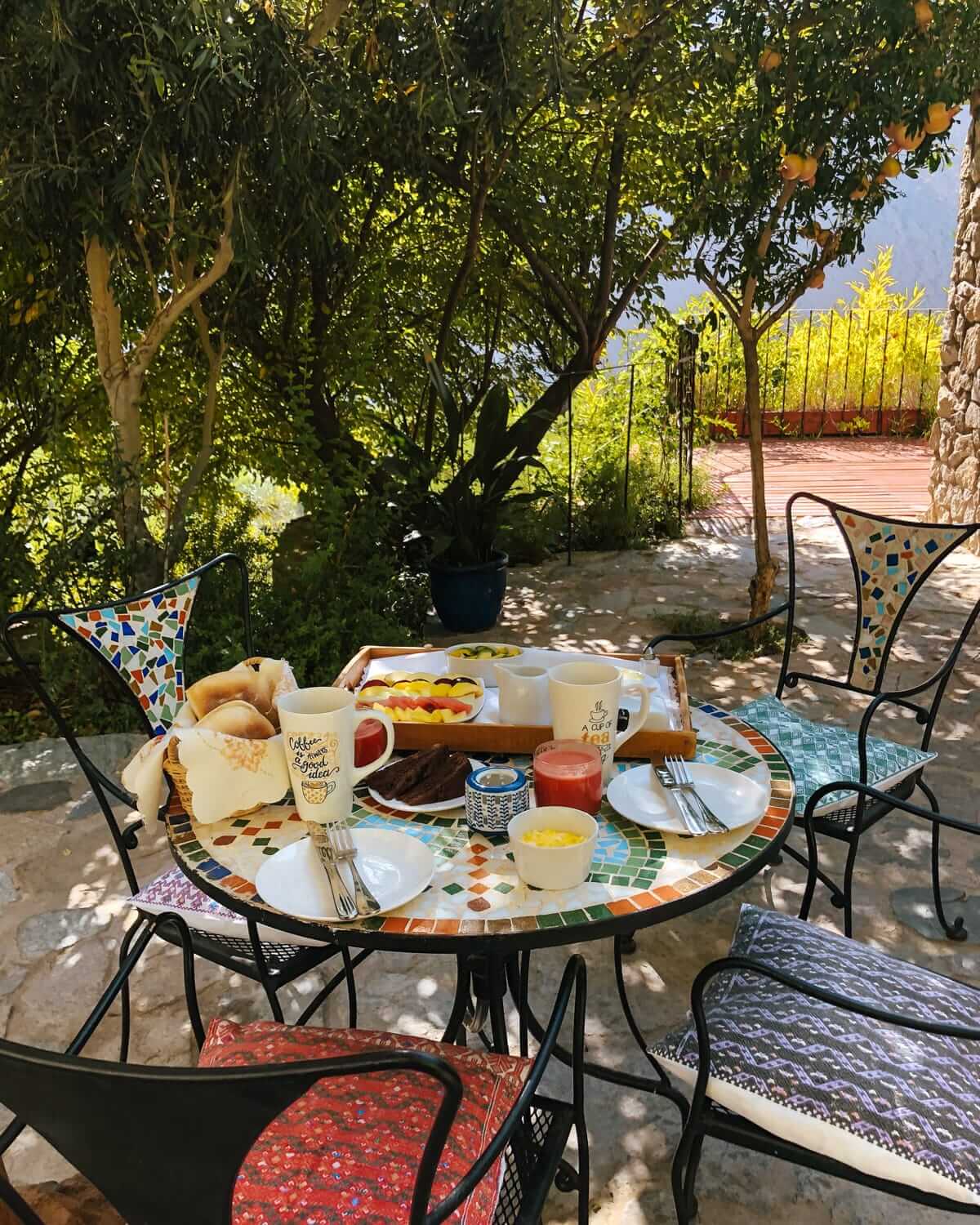 Breakfast on a mosaic-tiled table in a lush garden at Cabanas Caballieri, with fresh juice, pastries, and coffee.