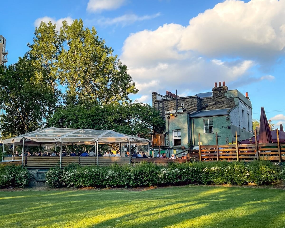 A London pub garden on a sunny day with people seated under a clear canopy, reflecting classic English pub culture.