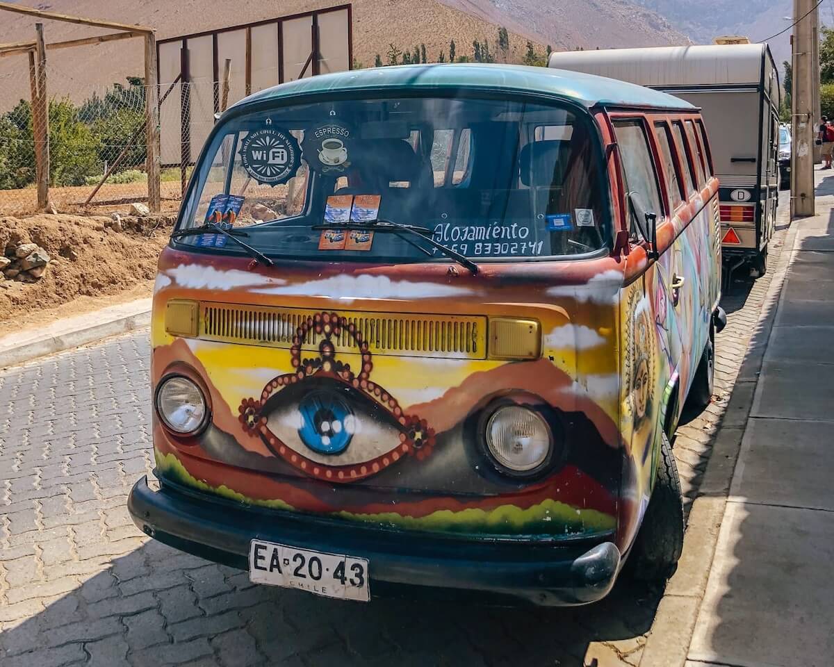 A colorful, hand-painted vintage Volkswagen van with an all-seeing eye design parked on a street in Pisco Elqui.