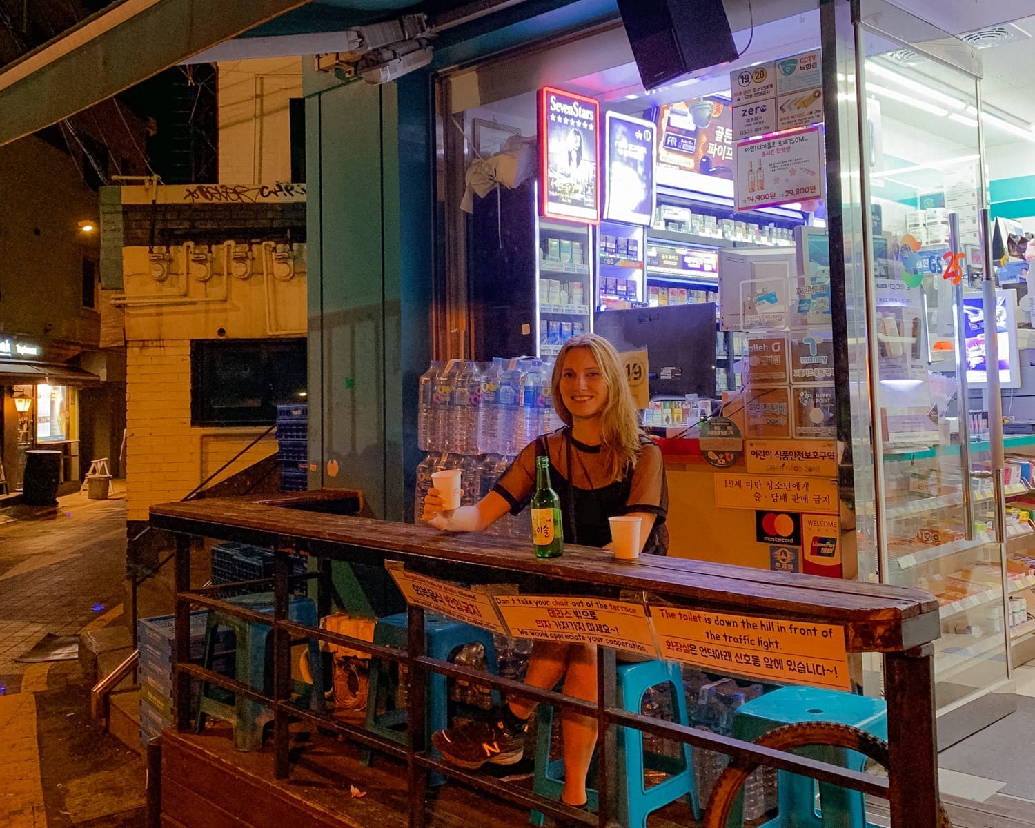 Cec enjoying a drink of soju outside a convenience store at night, a common social scene in Korea's buzzing nightlife.