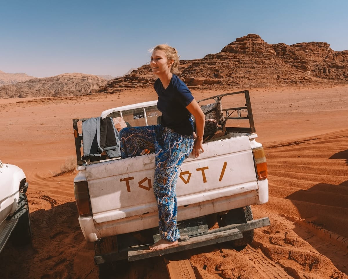 Cec climbing into the back of an old white Toyota pickup truck in the vast Wadi Rum desert.