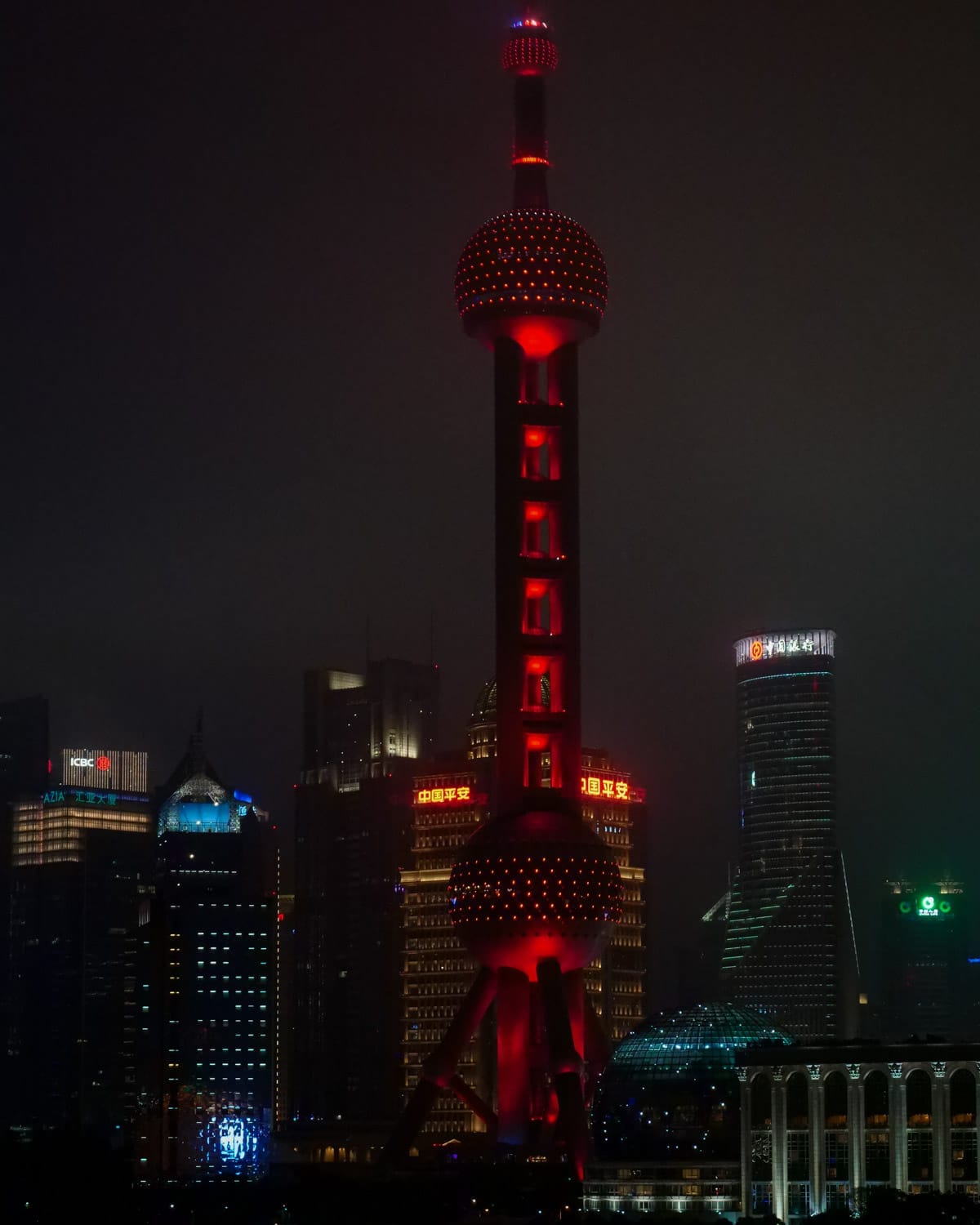 The Oriental Pearl Tower in Shanghai glows red against a dark night sky, surrounded by illuminated skyscrapers.