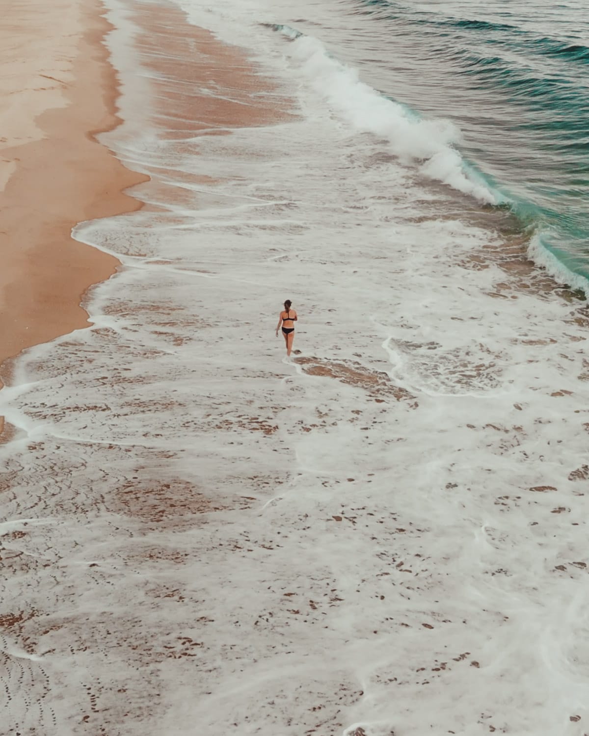 Drone shot of Cec walking along the shoreline in Cap Ferret with waves washing over the sand.