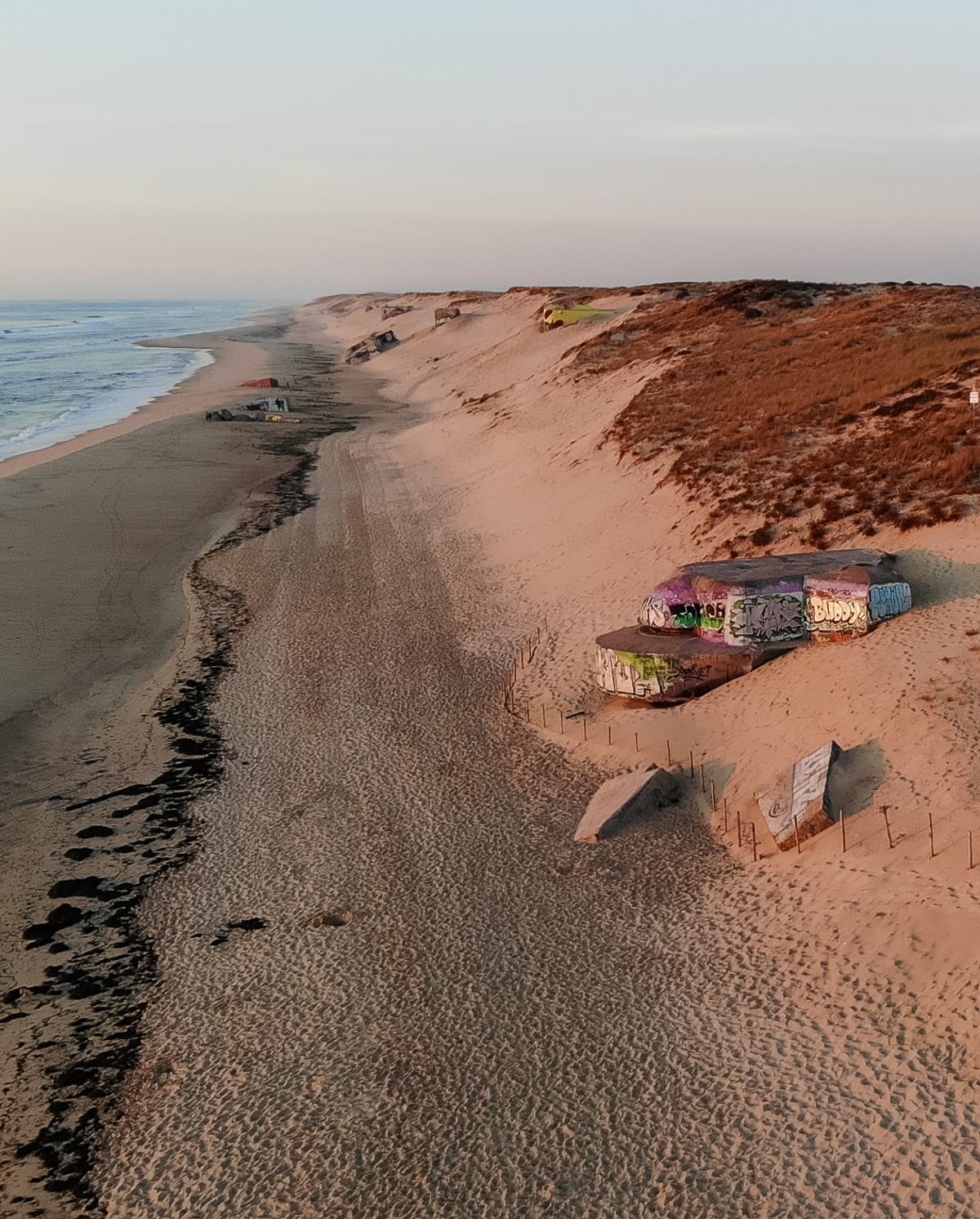 Graffiti-covered World War II bunkers partially buried in the sand along Cap Ferret’s Atlantic coast at sunset.