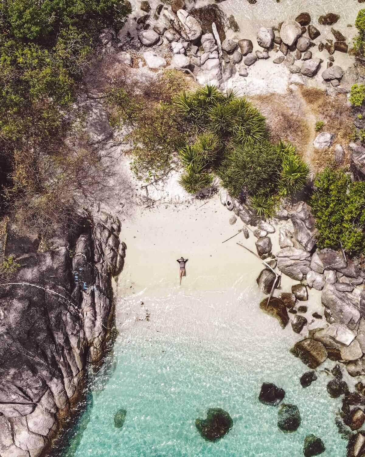 Cec lies on the remote sandy beach of an islet near Koh Lipe, surrounded by turquoise water, granite rocks, and lush green tropical foliage