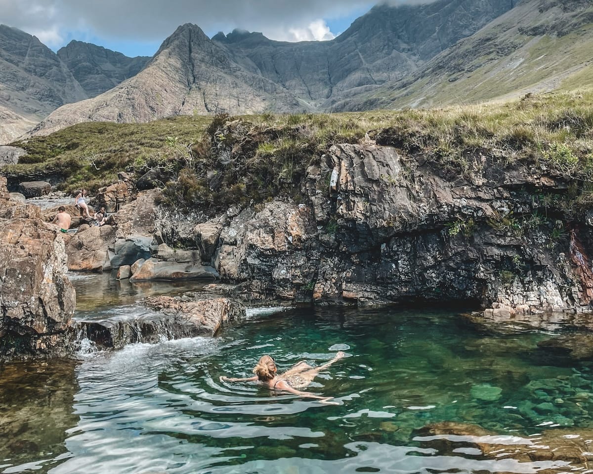 Cec swims in the crystal-clear Fairy Pools on the Isle of Skye, surrounded by rugged mountain peaks and rocky cliffs.