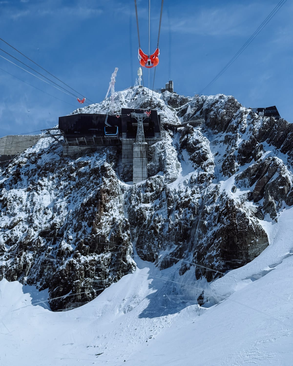 Cable car ascends snowy peaks up to Gornergrat Station, Switzerland against a backdrop of rugged alpine cliffs.