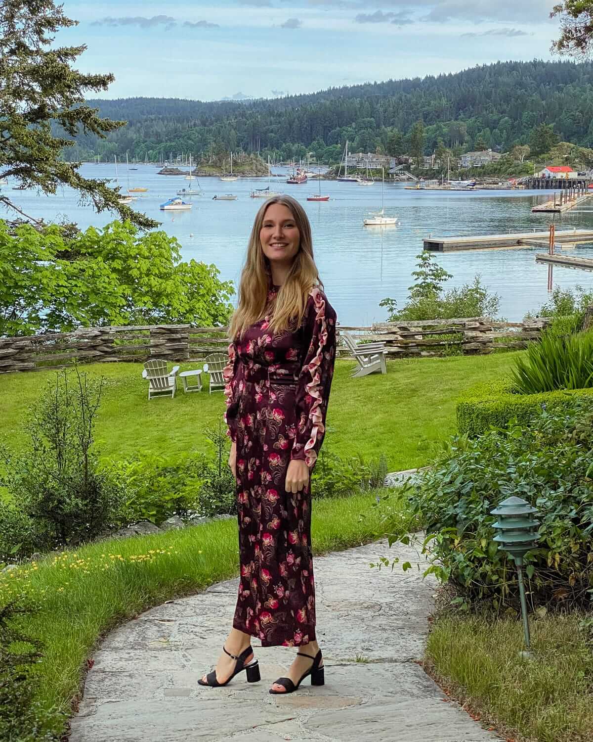 Cec standing in a floral dress at Hastings House grounds with lush greenery and Ganges Harbour behind.