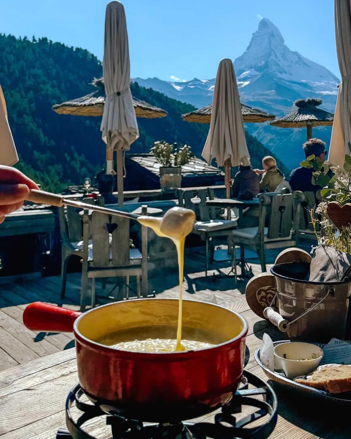 Cheese fondue being enjoyed on an alpine terrace with a view of the Matterhorn in Switzerland.