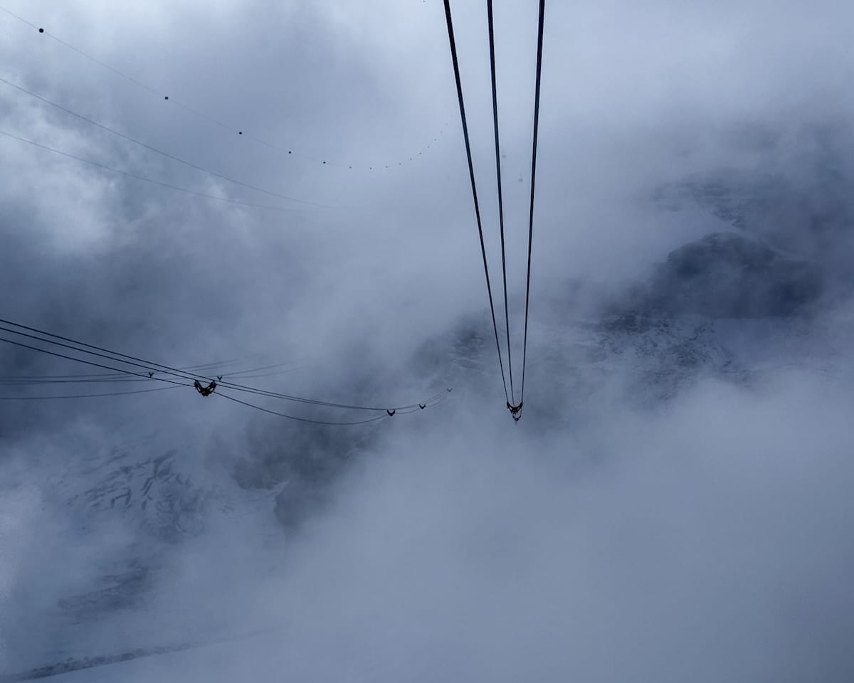 Suspension cables from Gornergrat Station disappear into thick fog and mist over the snowy Swiss Alps.
