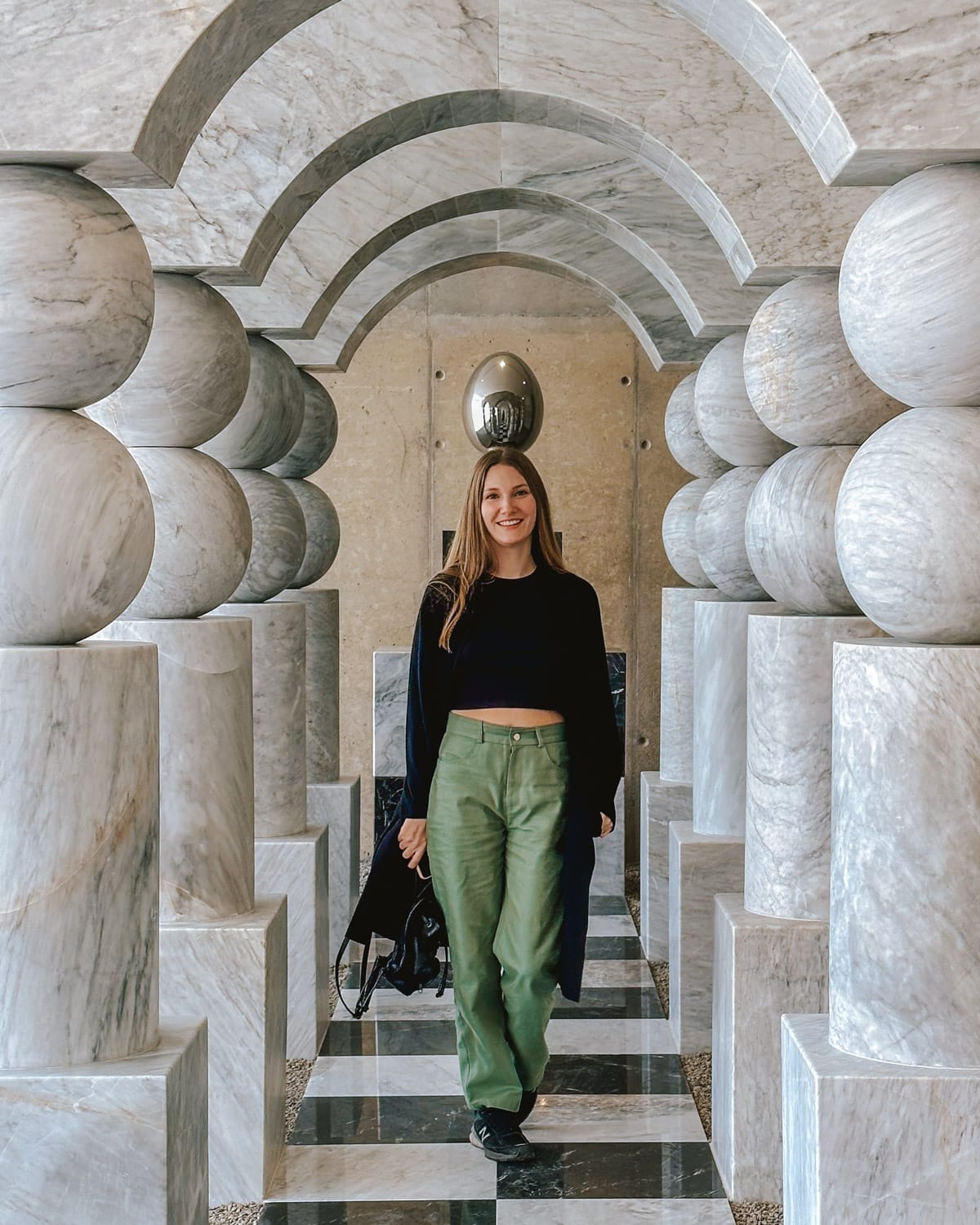 Cec walking through a sculptural marble hallway with arched ceilings and checkered floors at an exhibition for Art Week in Mexico City.