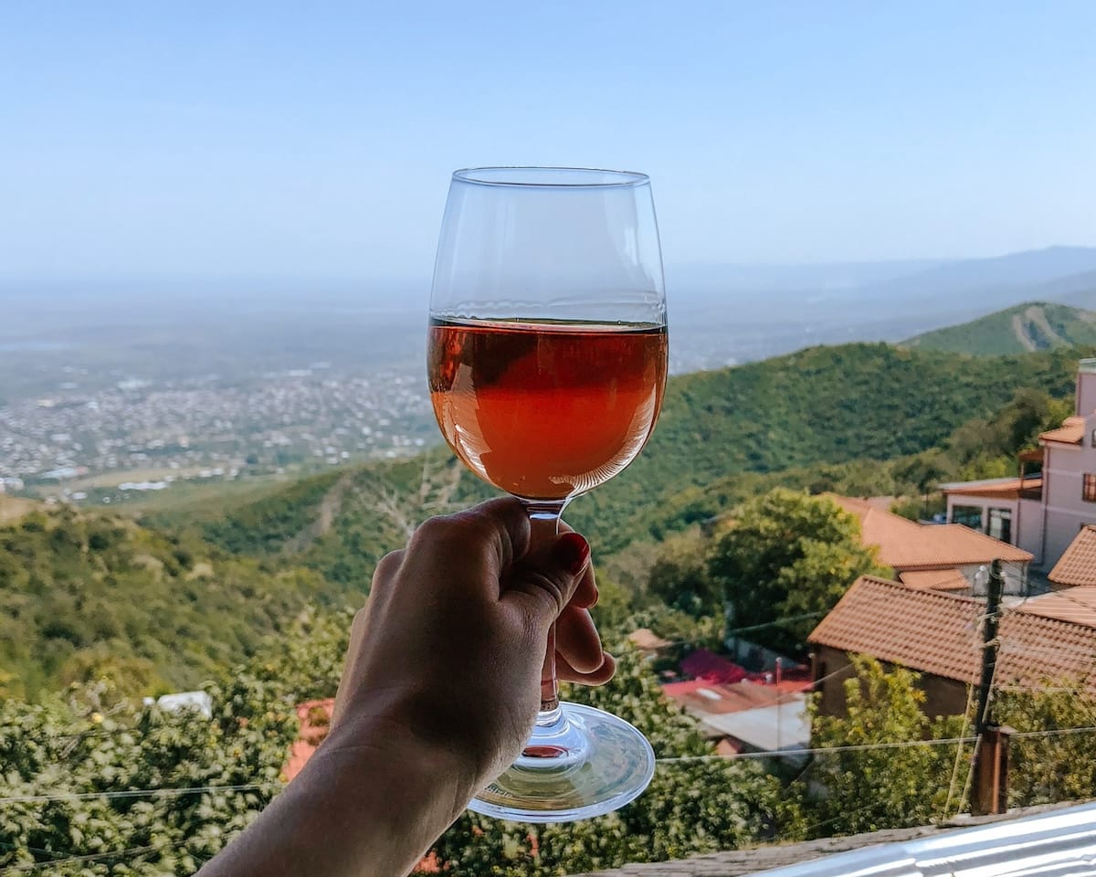 Hand holding a glass of Georgian wine with sweeping views of the Kakheti countryside, a region famed for 8,000 years of winemaking.