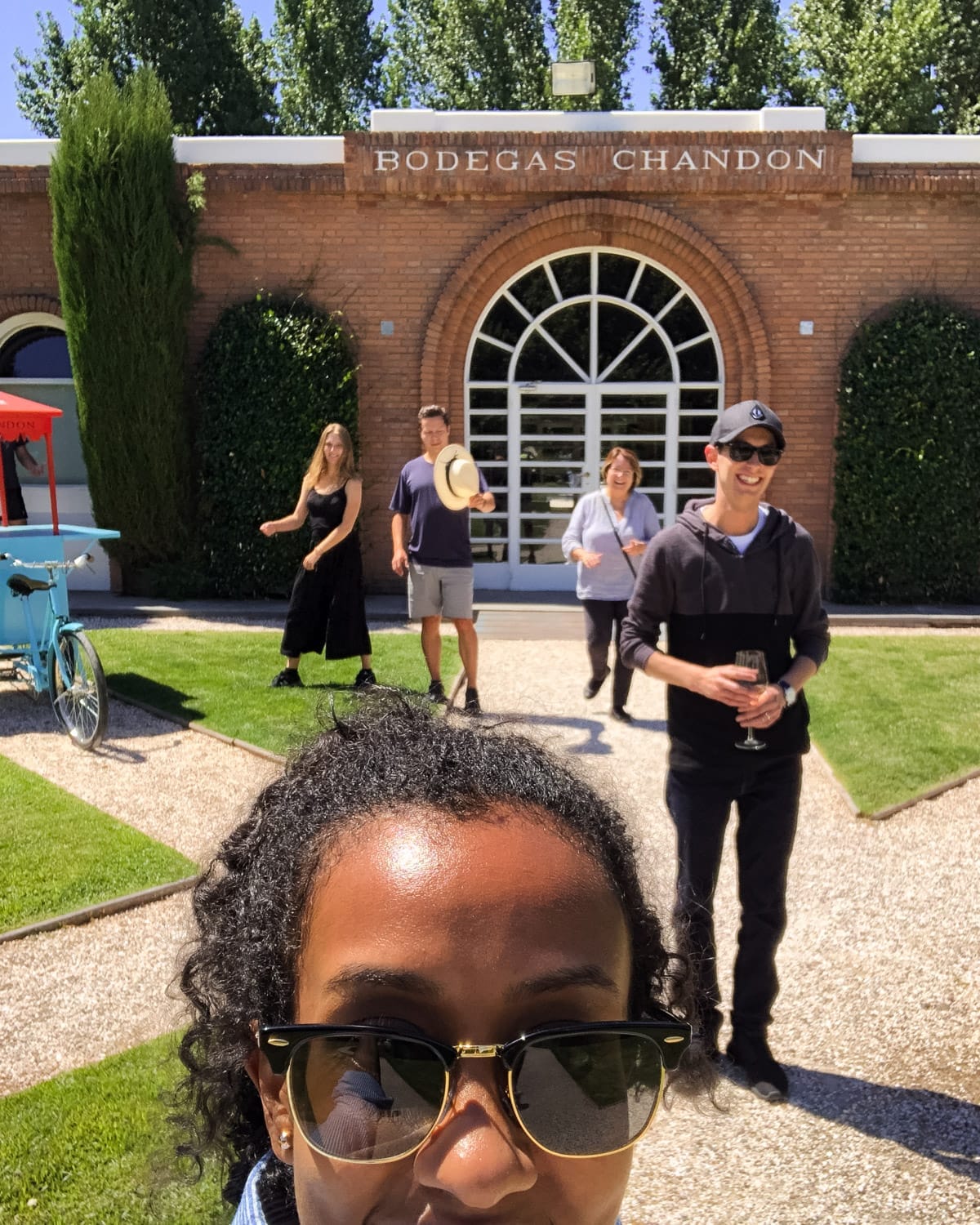 Woman takes selfie in front of Bodegas Chandon while four friends walk behind her, smiling in the sunshine.