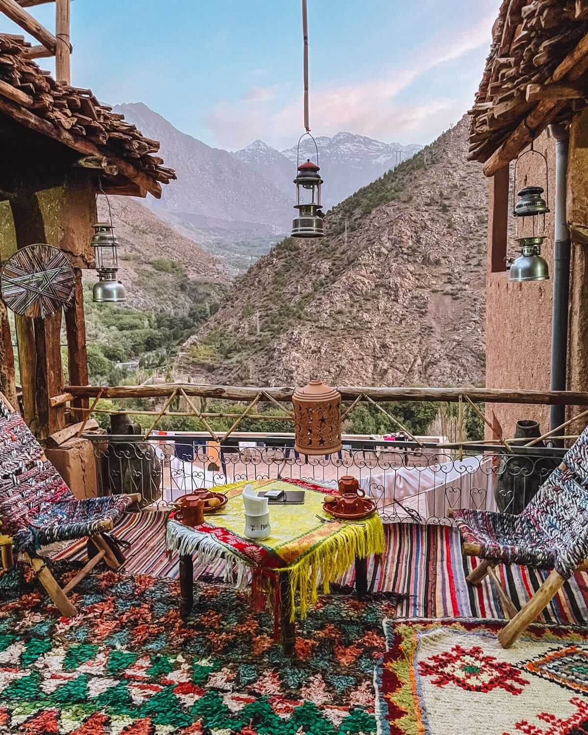 Rustic terrace at a Berber lodge in Morocco’s Atlas Mountains, with colourful rugs and mountain views at dusk.