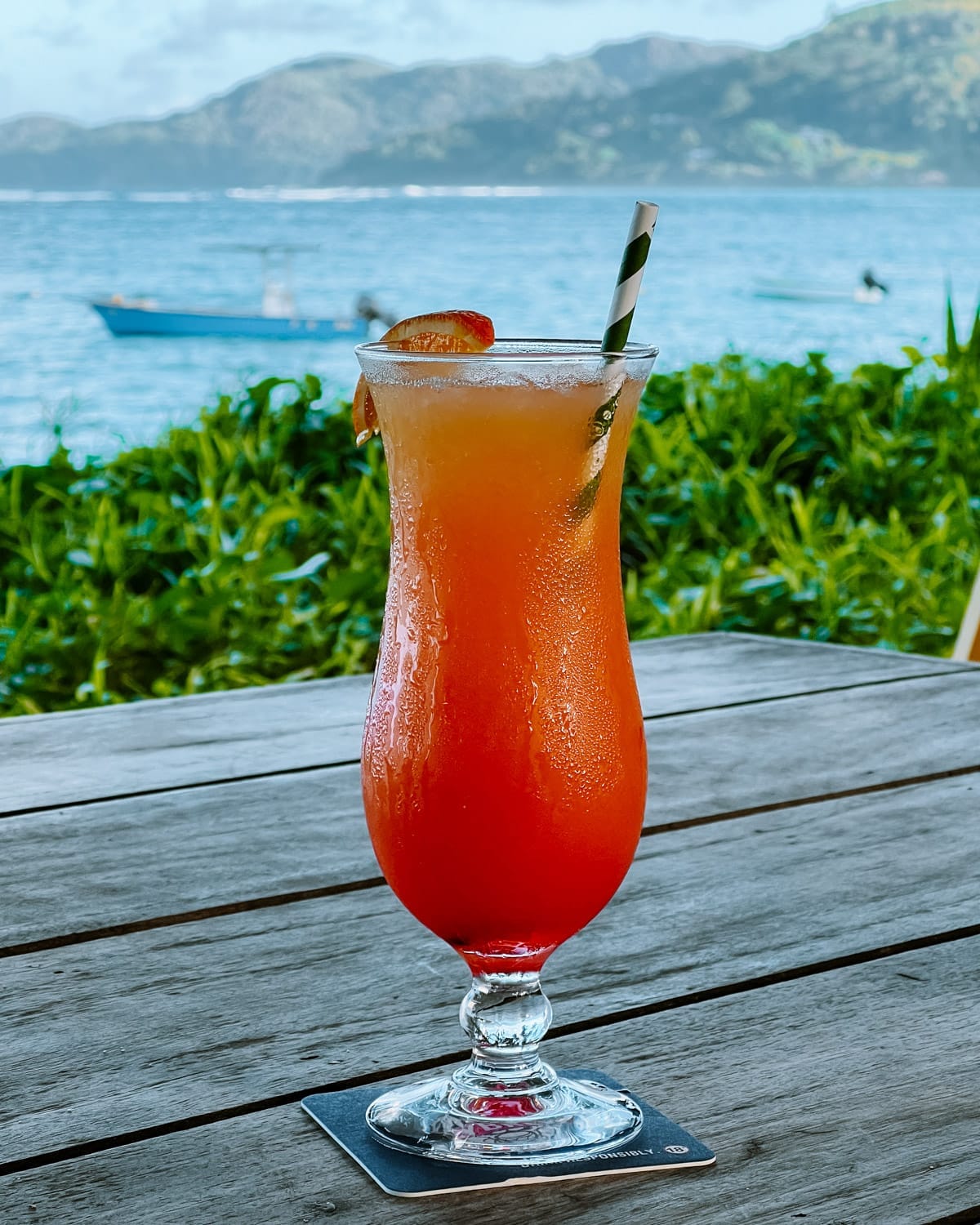 Bright tropical cocktail on a seaside table on Mahe Island with a view of the ocean and nearby hills.