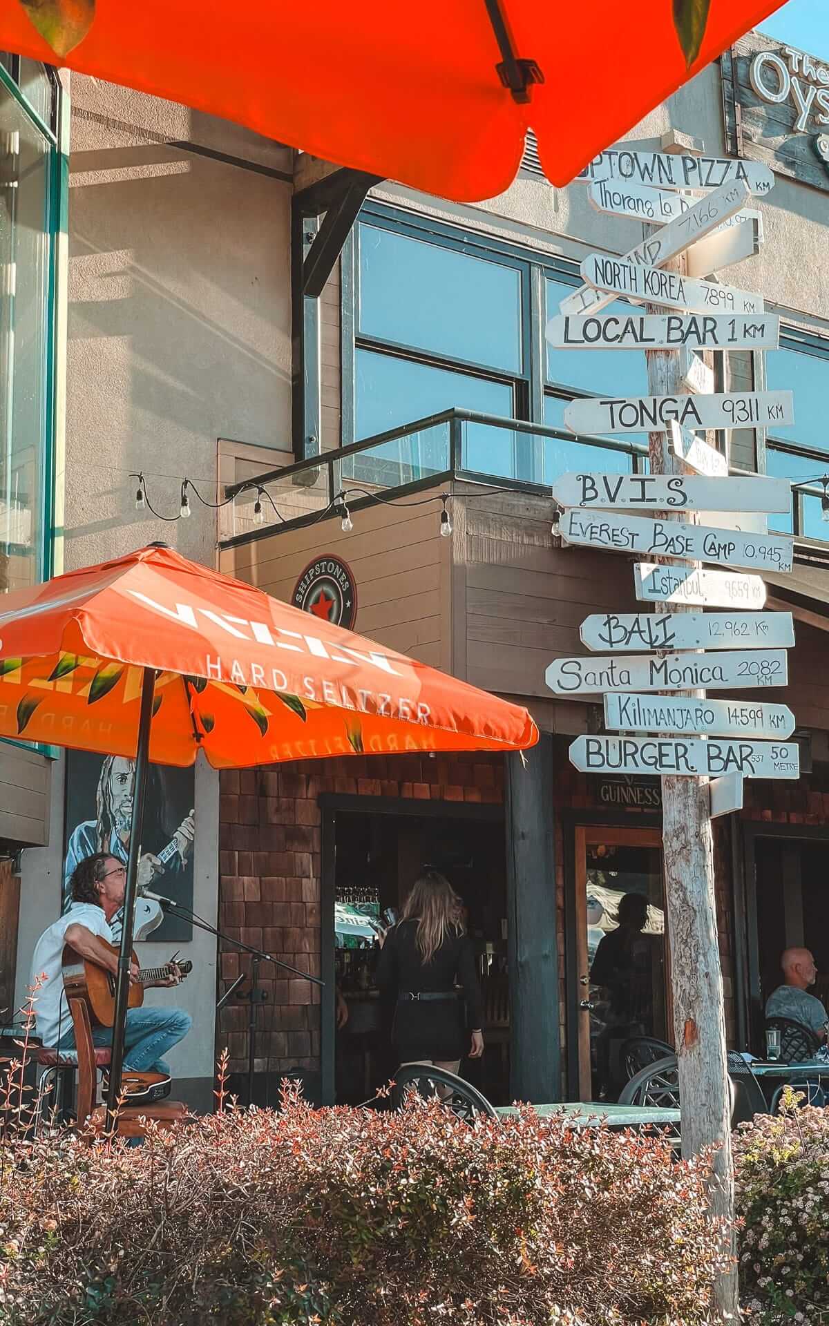  Outdoor live music at Oyster Catcher, with a directional signpost and an orange patio umbrella overhead.