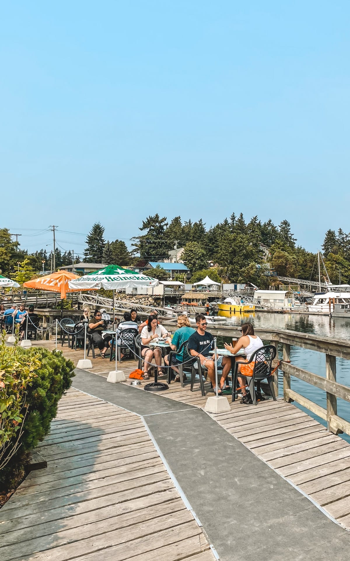 Diners enjoying sunny waterfront seating on the wooden patio deck at Oyster Catcher on Salt Spring Island.