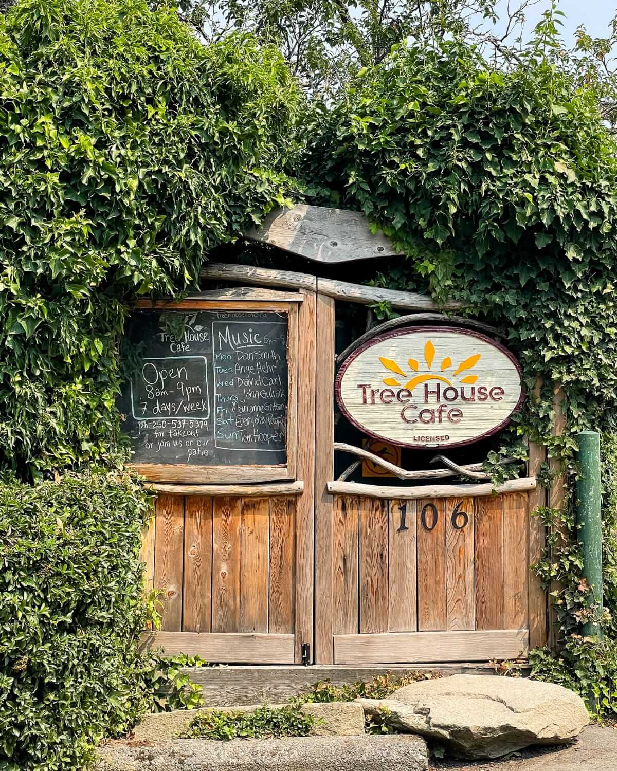 Rustic entrance of Tree House Cafe on Salt Spring Island, framed by greenery, with a chalkboard listing live music and hours.