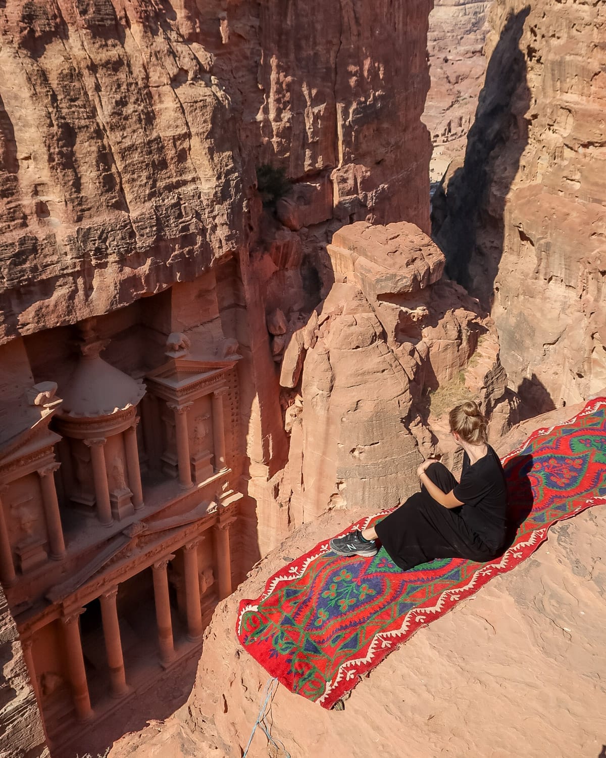 Cec sits on a red patterned rug overlooking Petra’s famous Treasury carved into rose-colored cliffs.