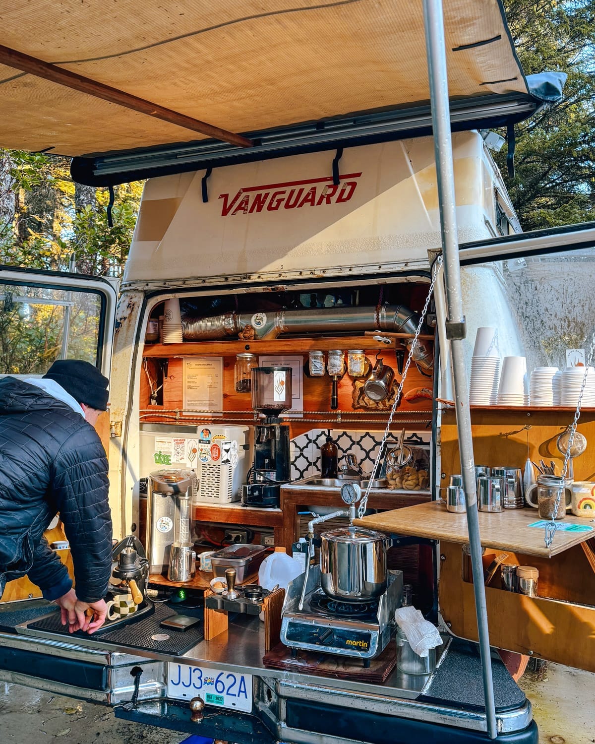 Campervan cafe set up in Tofino with coffee equipment, a barista, and rustic decor.