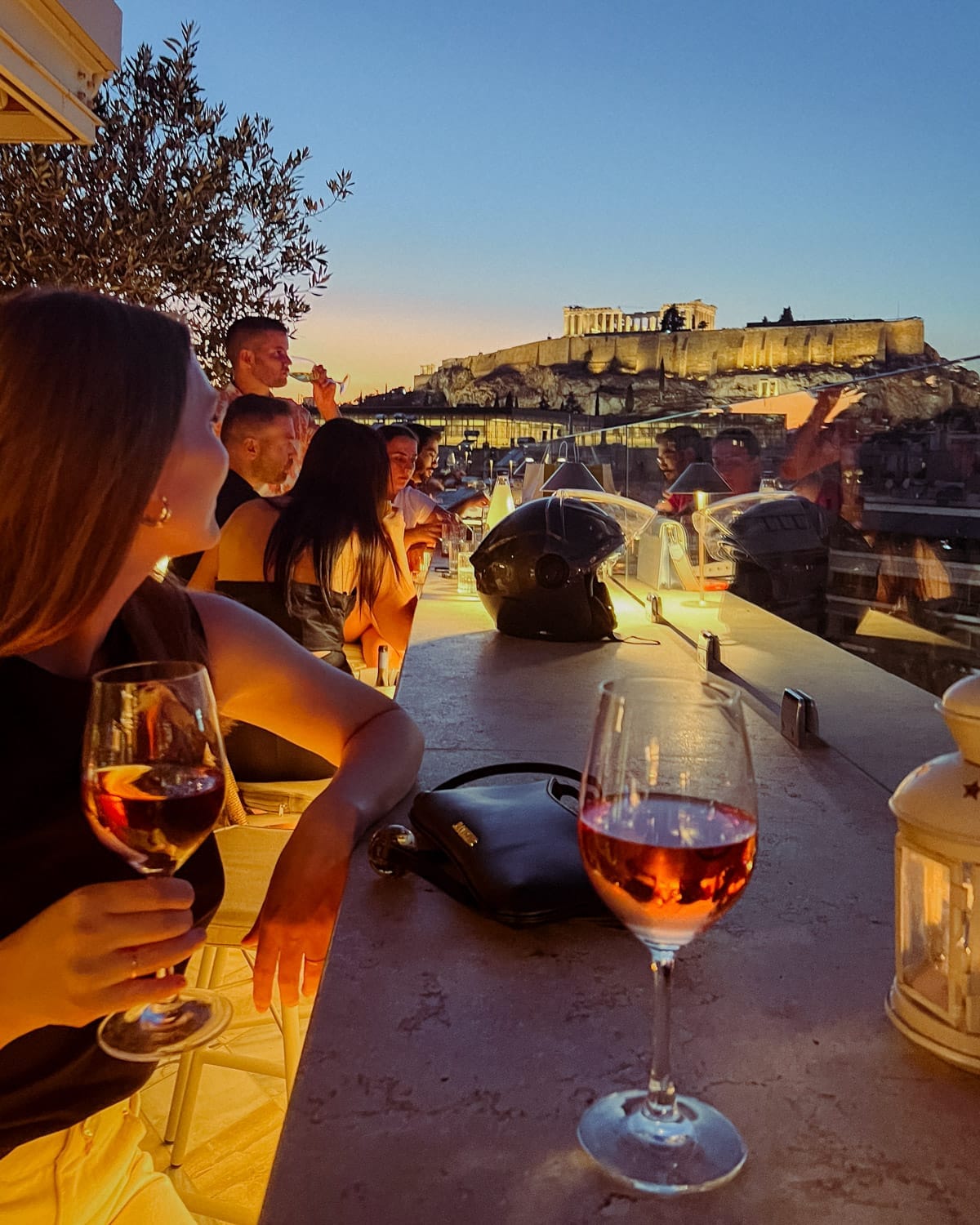 People enjoying sunset drinks with a view of the Acropolis from a rooftop bar in Athens.