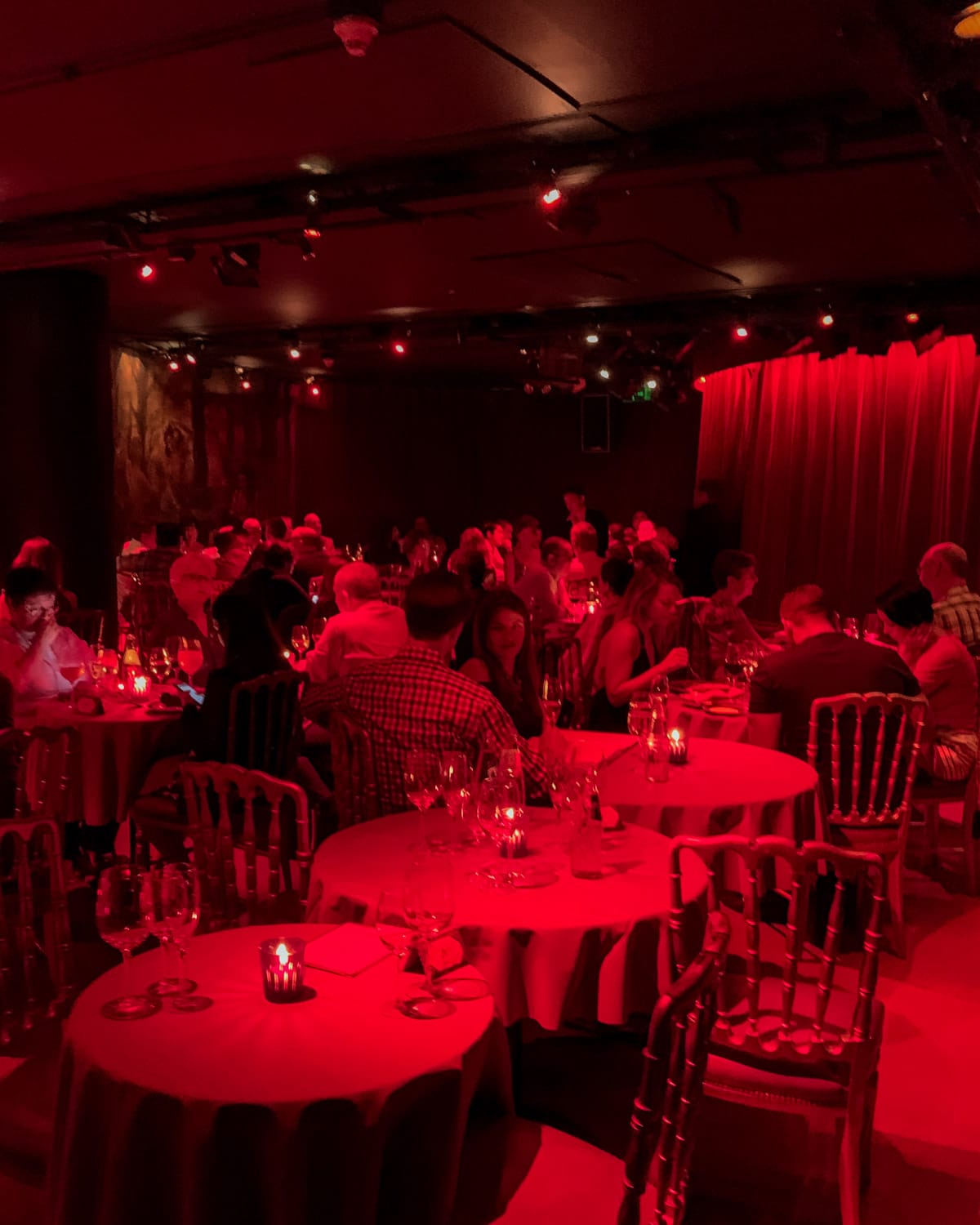 Intimate dinner theatre bathed in red light with round tables, guests dining waiting for the Rojo tango performance to begin. 