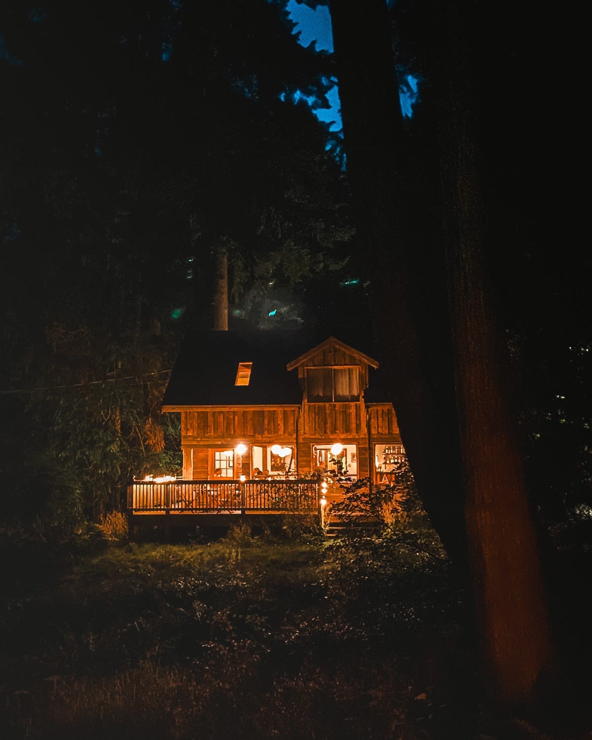 Cozy log cabin restaurant glowing with warm lights at night, nestled among tall trees on Galiano Island.