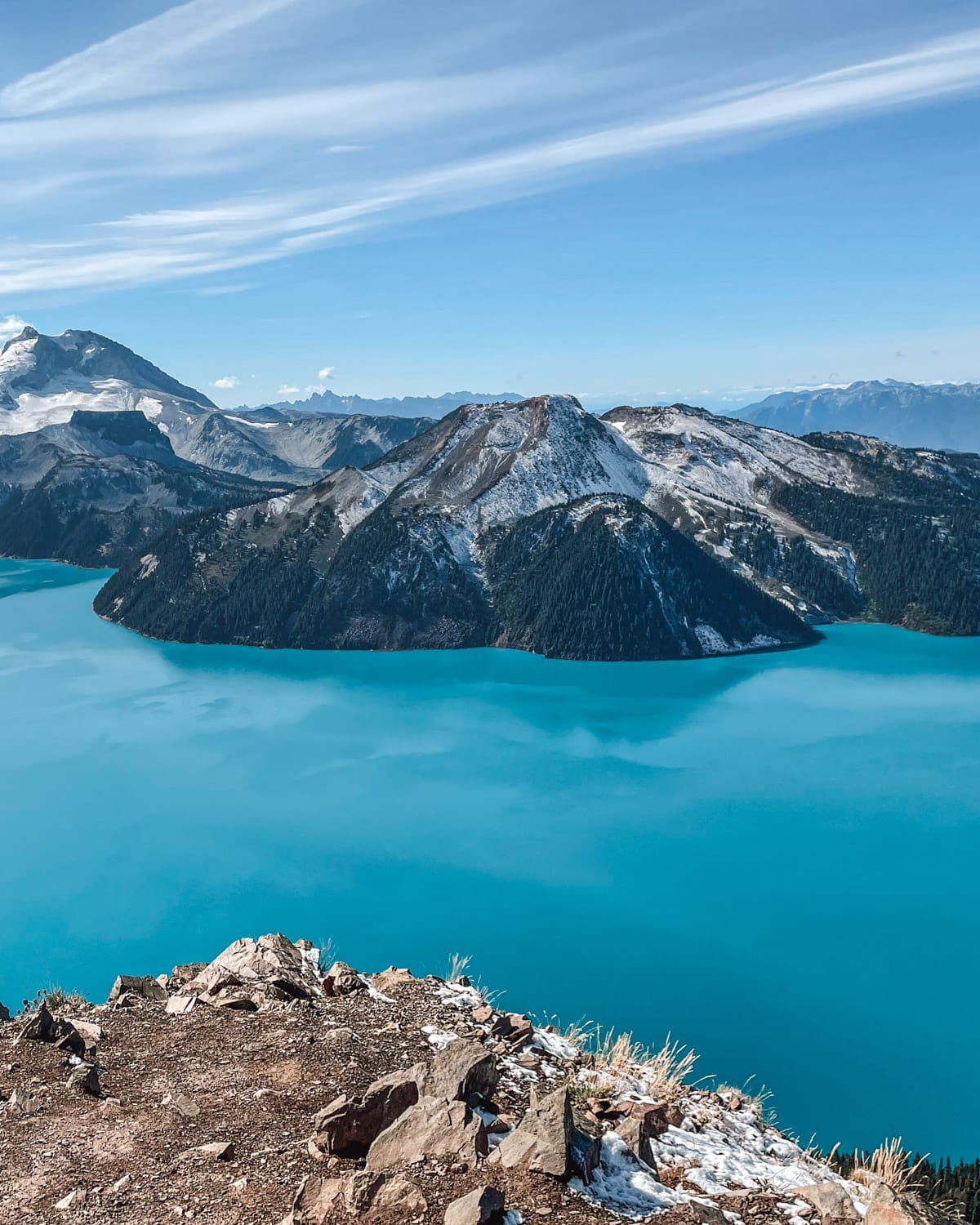 Stunning view of Garibaldi Lake’s vivid turquoise waters surrounded by snow-capped mountains and stratovolcanoes under a clear blue sky.