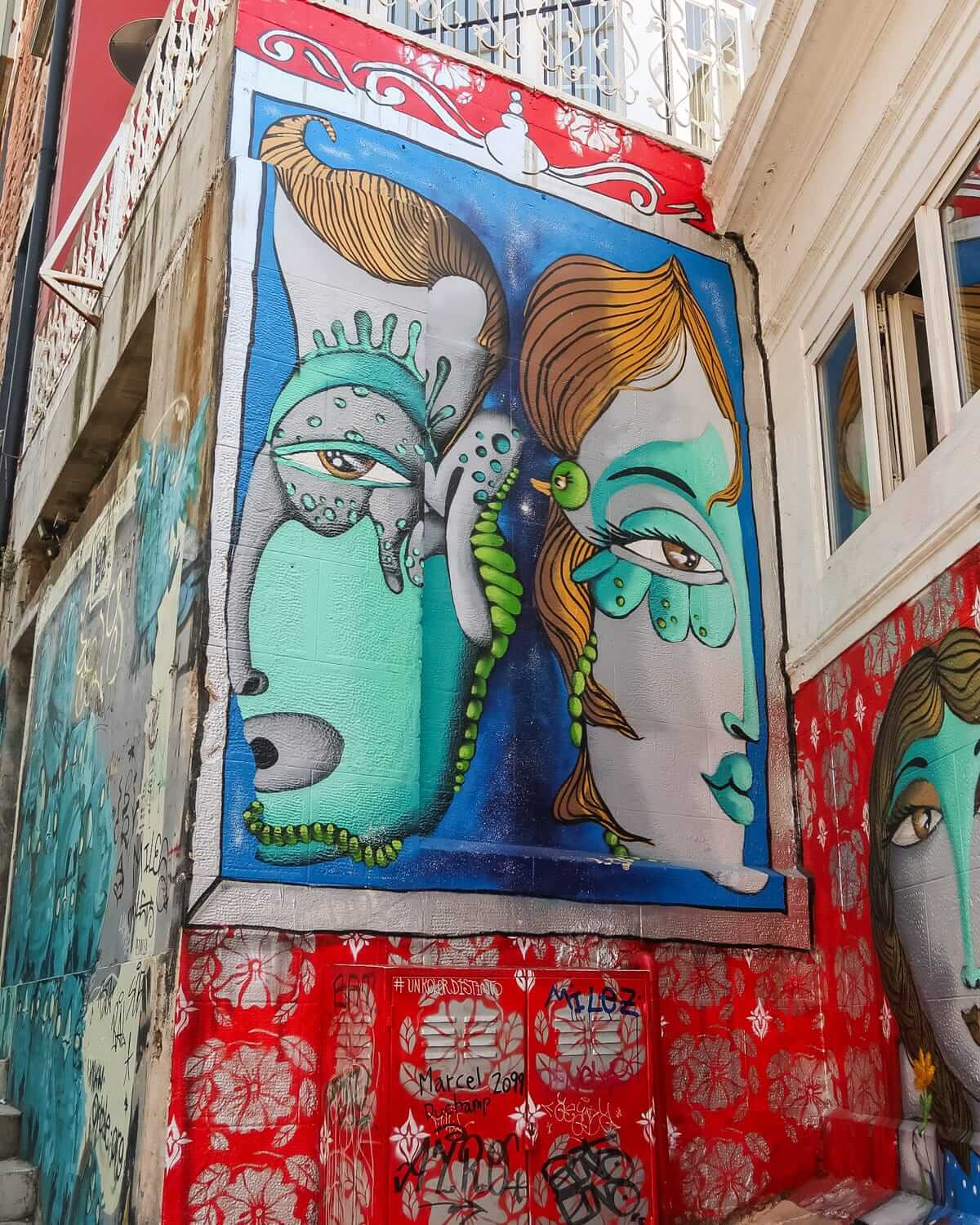 Colourful mural of two abstract faces on a red and blue graffiti-covered wall in Valparaíso.