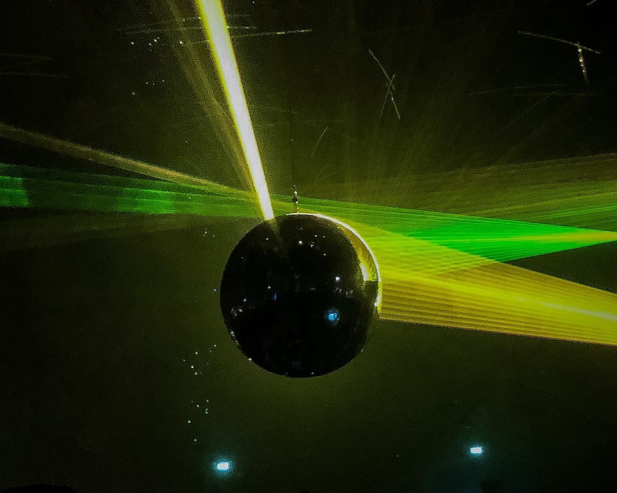 A disco ball reflects green and yellow laser lights in a dark nightclub setting at Awakenings Festival in Amsterdam.