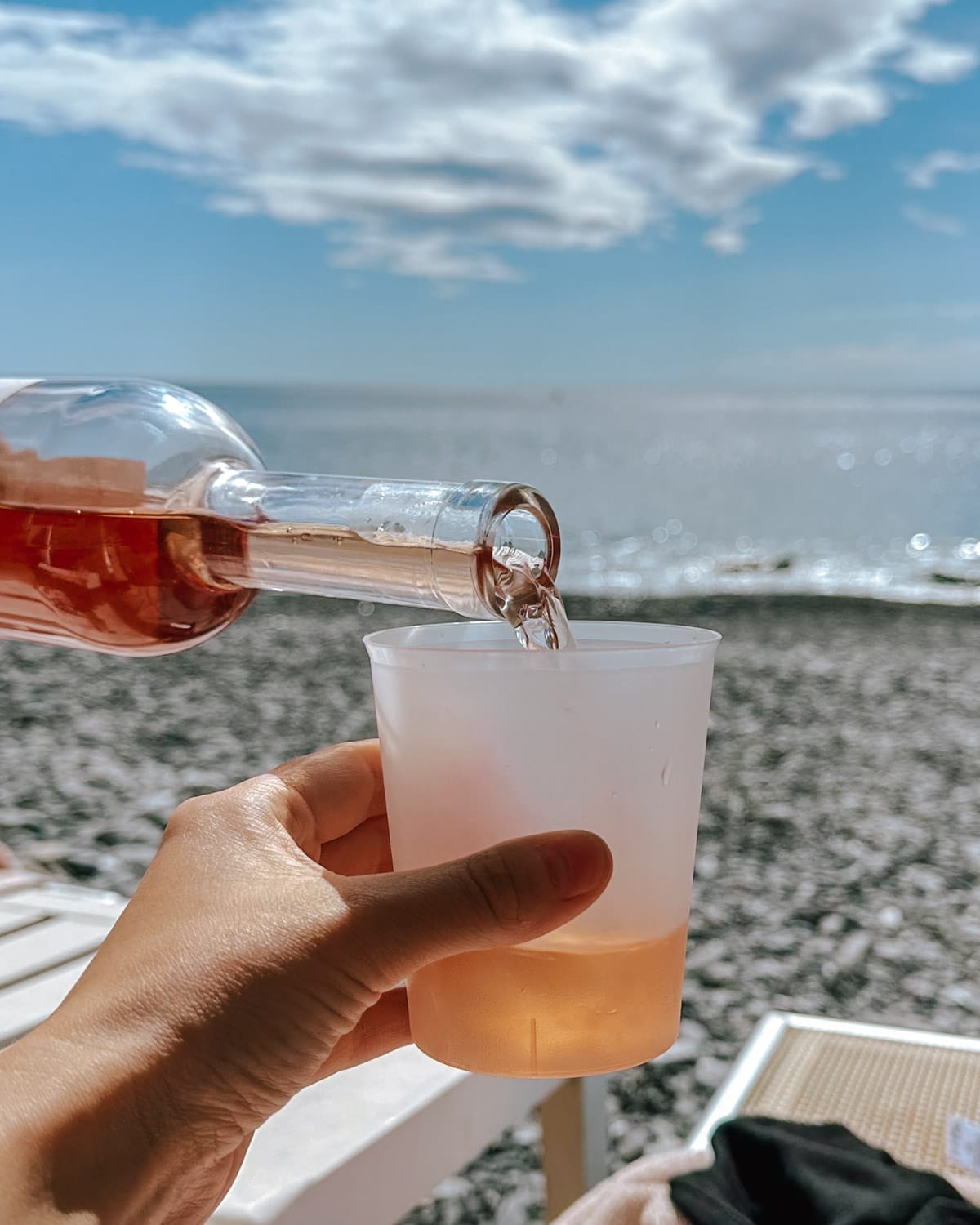 Rosé wine is poured into a plastic cup at a pebble beach on the Italian Riviera.