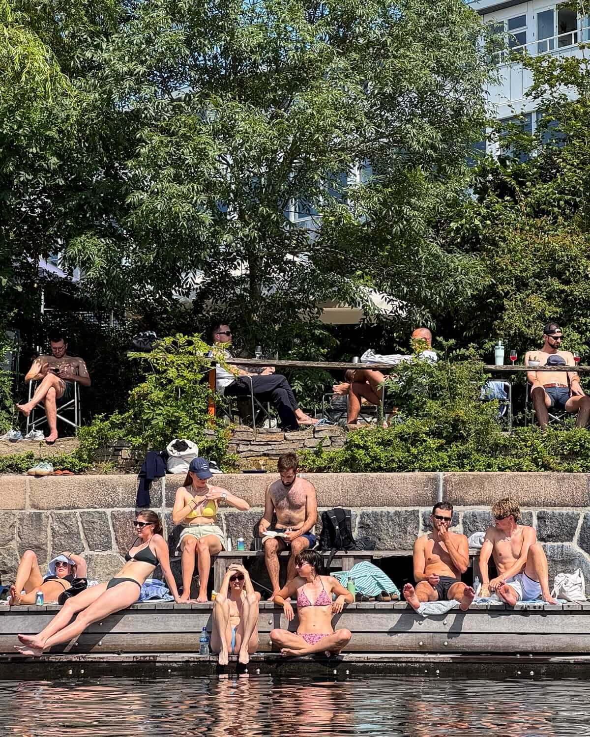 Locals sunbathe and relax on the canal edge in Copenhagen on a warm summer day.