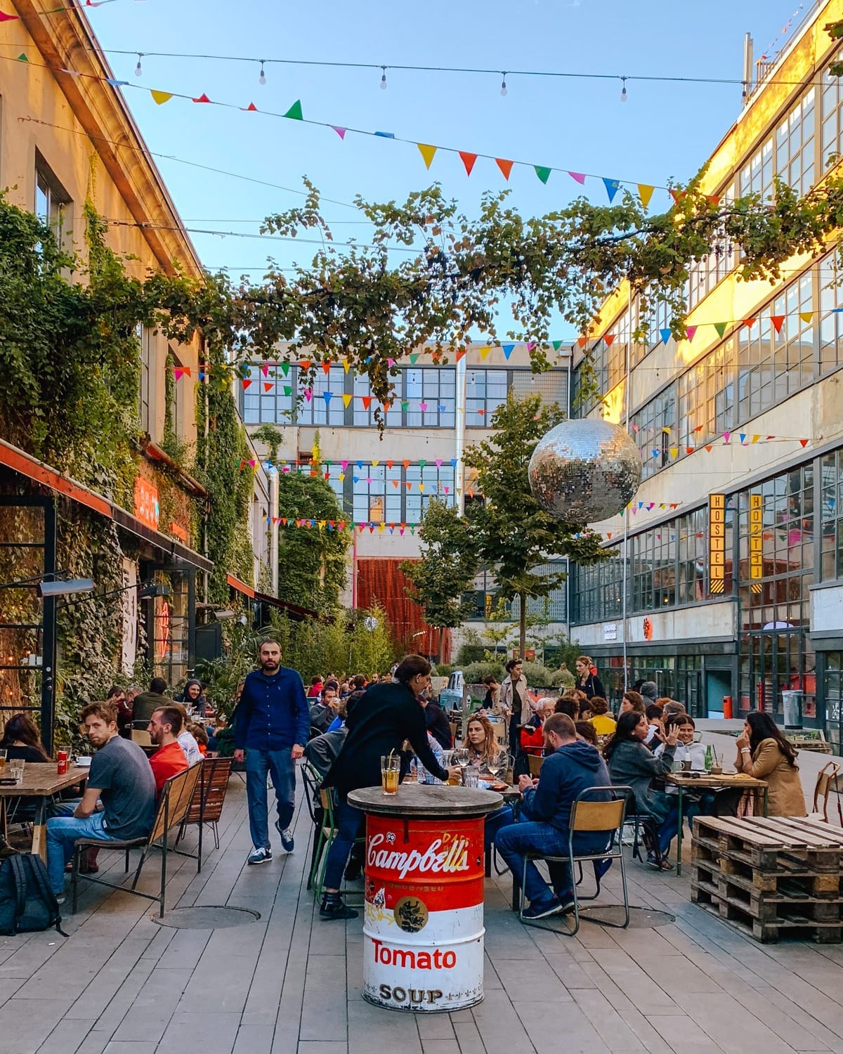 The lively Fabrika courtyard in Tbilisi filled with locals enjoying drinks, am Andy Warhol-inspired Campbell's tomato soup can table and a large disco ball capturing the city’s creative, social spirit.