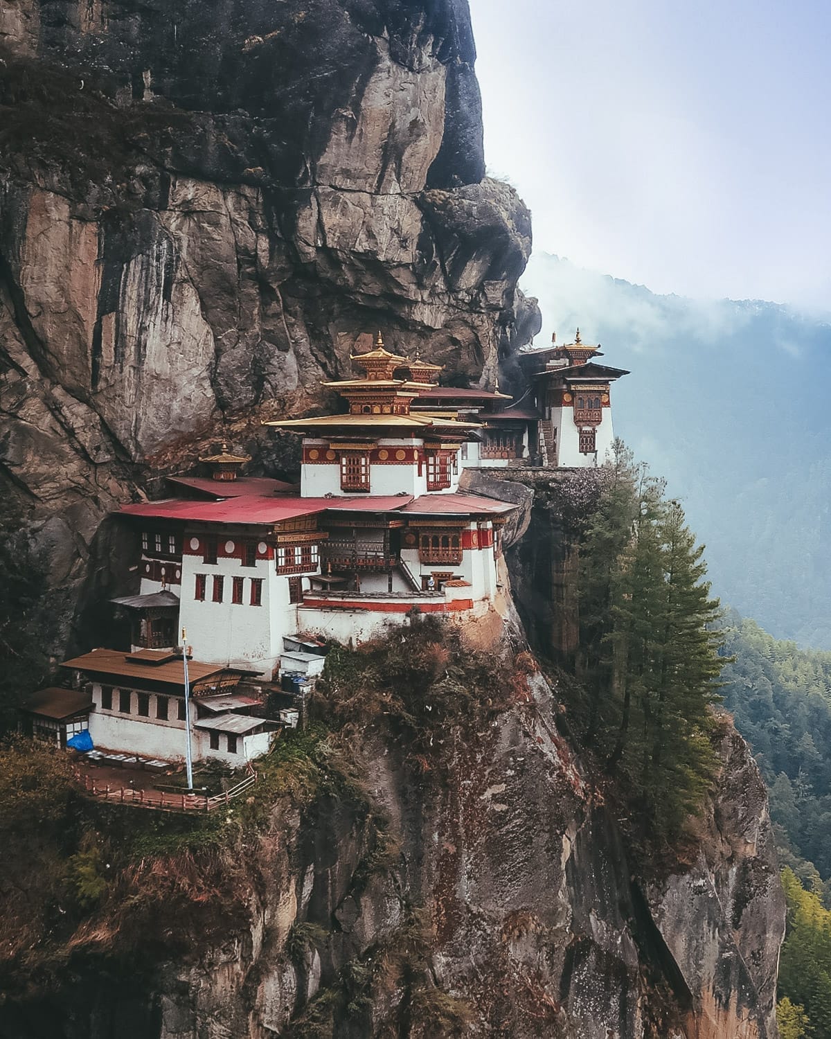 The Tiger’s Nest Monastery clings to the edge of a steep cliff, surrounded by forest and soft mist in Bhutan’s mountains.