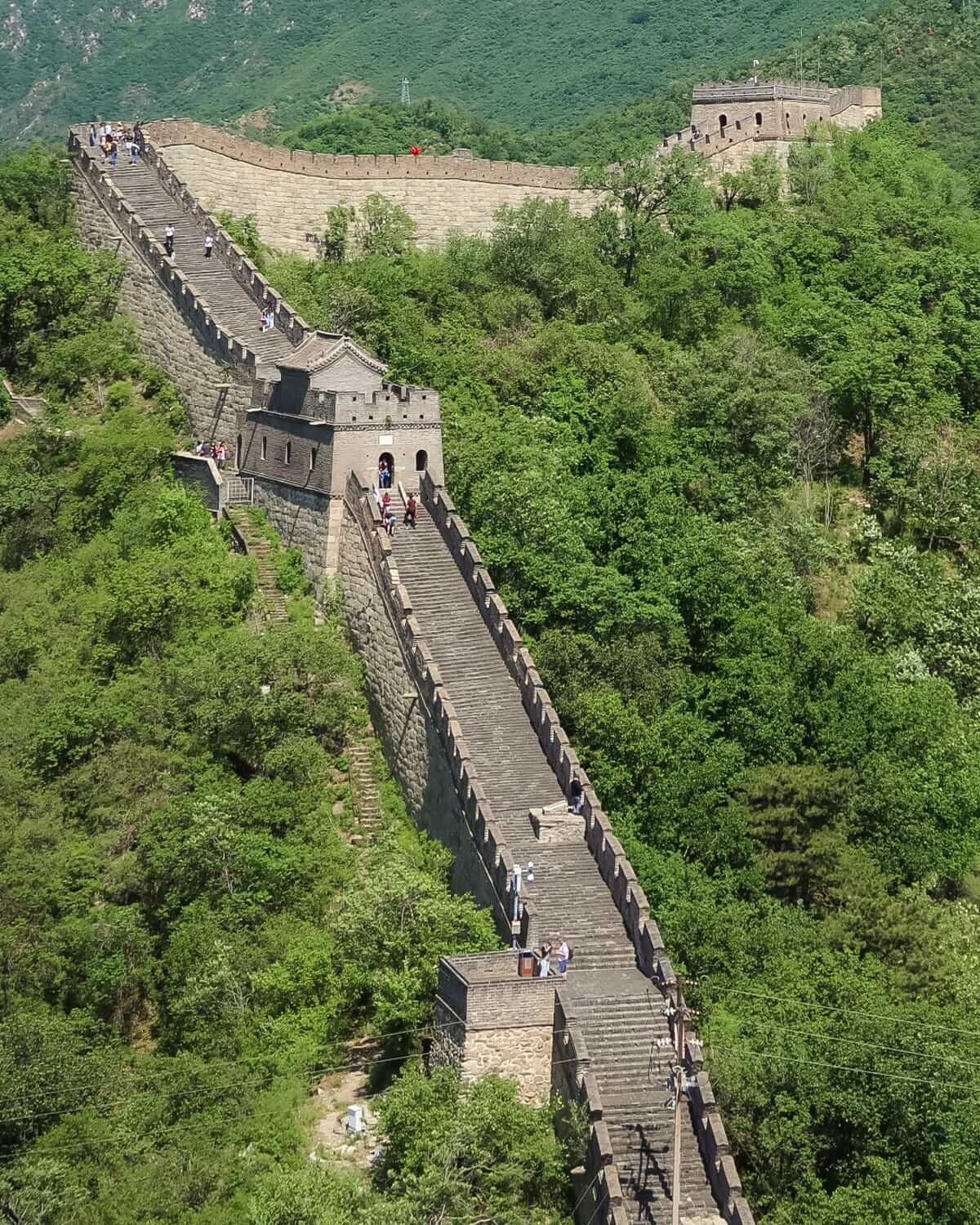 The Great Wall of China winds through lush green hills, dotted with tourists exploring the landmark