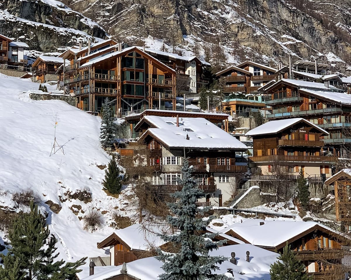 Charming wooden chalets dot a snowy hillside in Zermatt, Switzerland, with the rocky Alps rising behind.