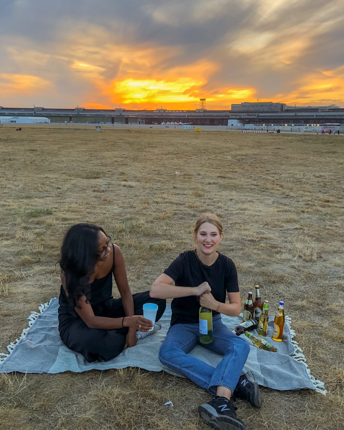 Cec and her friend picnic with drinks at sunset on Berlin’s Tempelhofer Feld, a historic airfield turned public park.