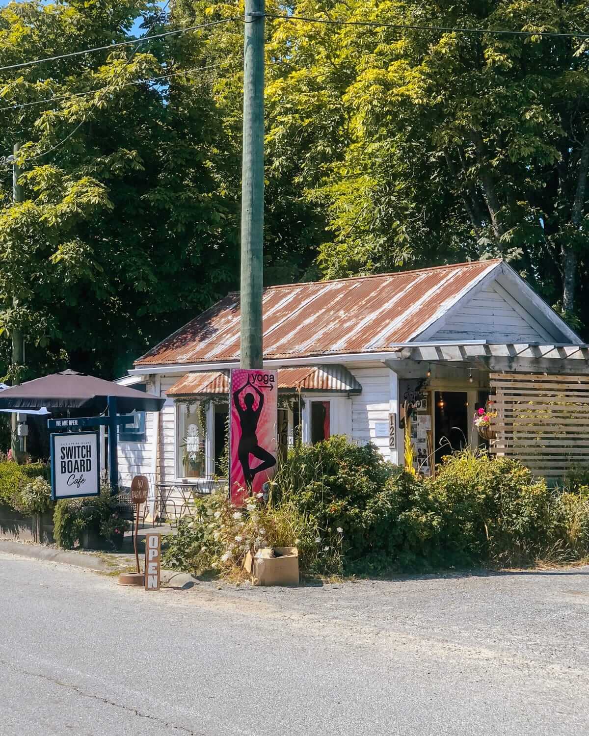 Exterior of Switchboard Cafe with a rusted tin roof, lush greenery, and a yoga banner out front.