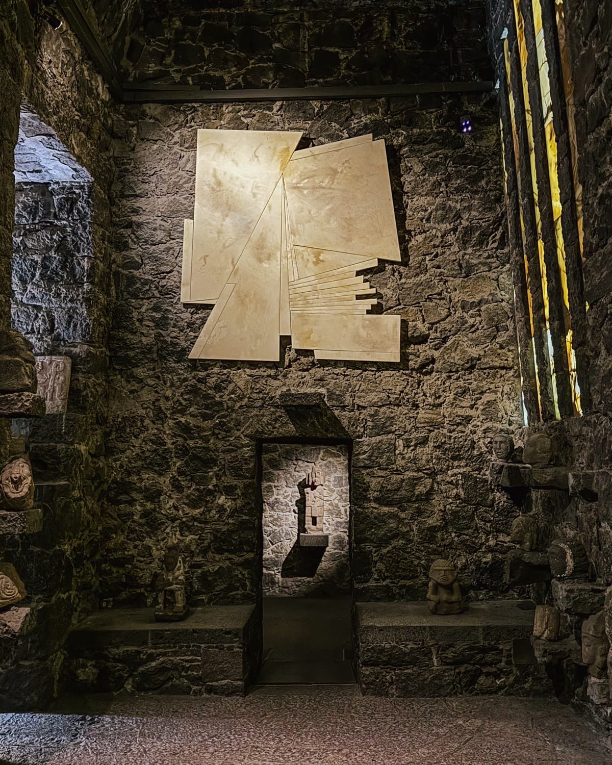 Shadowy interior of Museo Anahuacalli in Mexico City with pre-Hispanic sculptures and modern art.